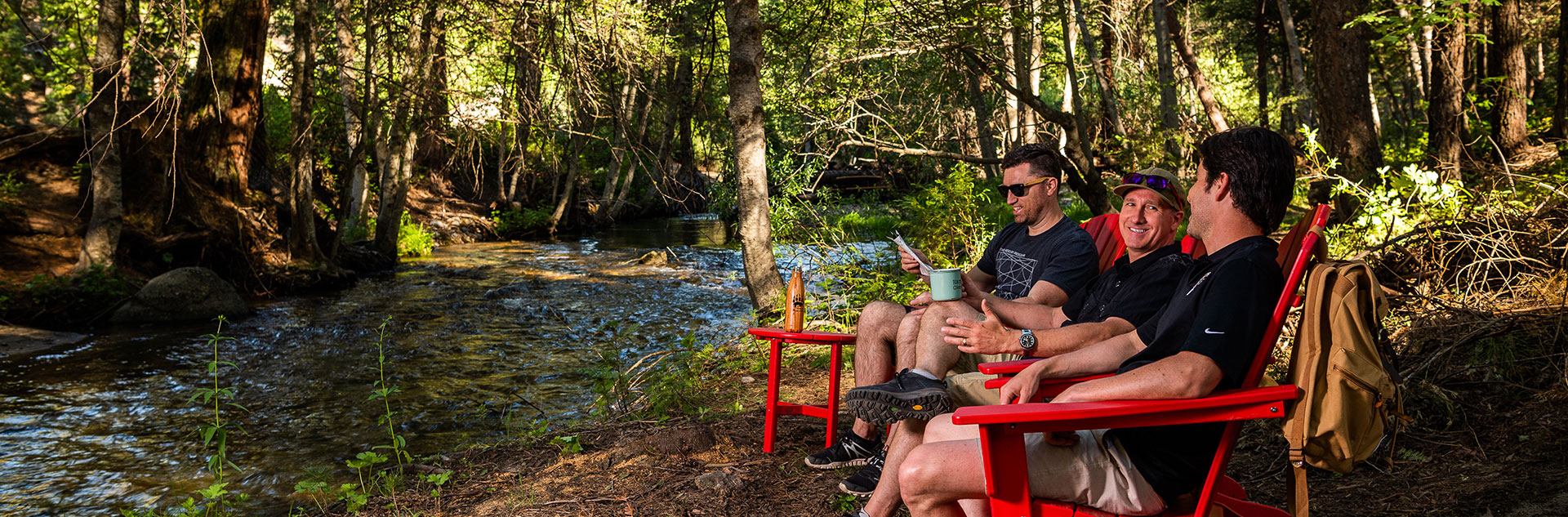 Three men sitting on red wooden chairs enjoying a chat out in the outdoors.