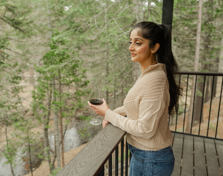 A guest enjoying a glass of wine on the porch of her Explorer Cabin at Yosemite