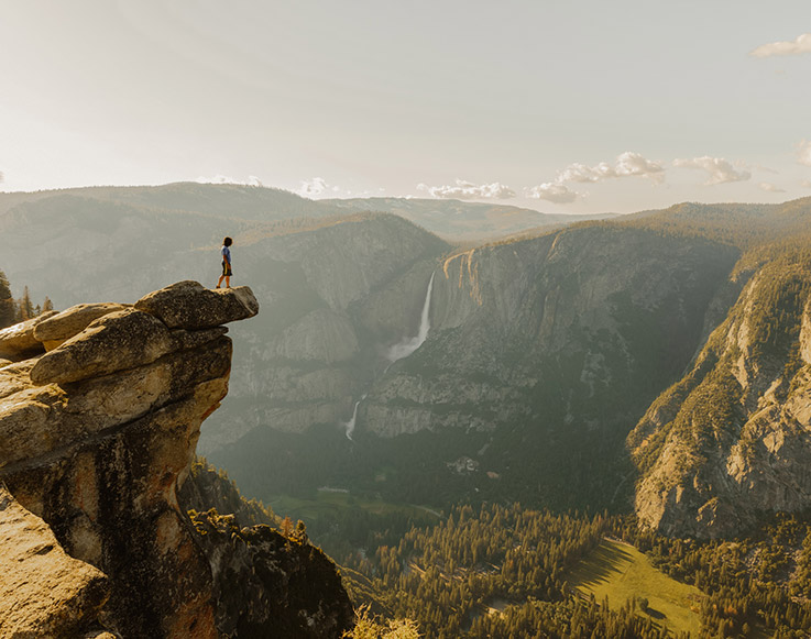 A brave Yosemite hiker standing on a rocky outcrop over the valley floor.